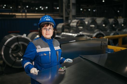 A woman in safety gear inspects metal sheets in a modern Russian industrial setting.